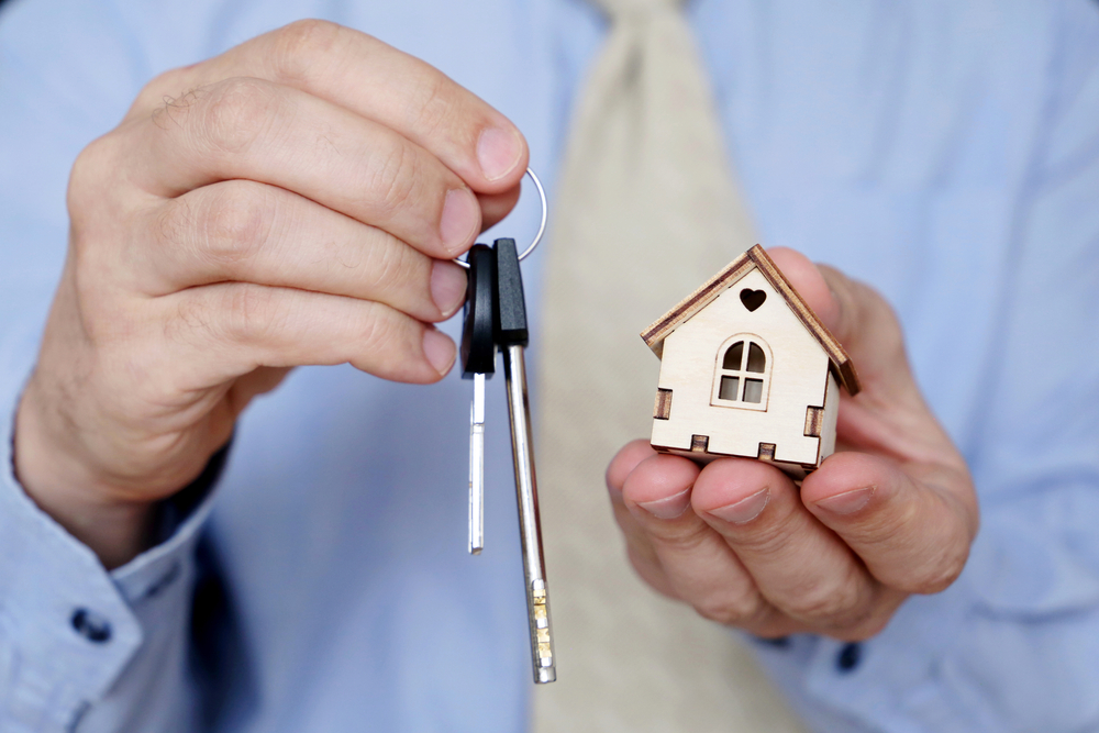 Real estate agent, apartment keys and wooden house in male hands.
